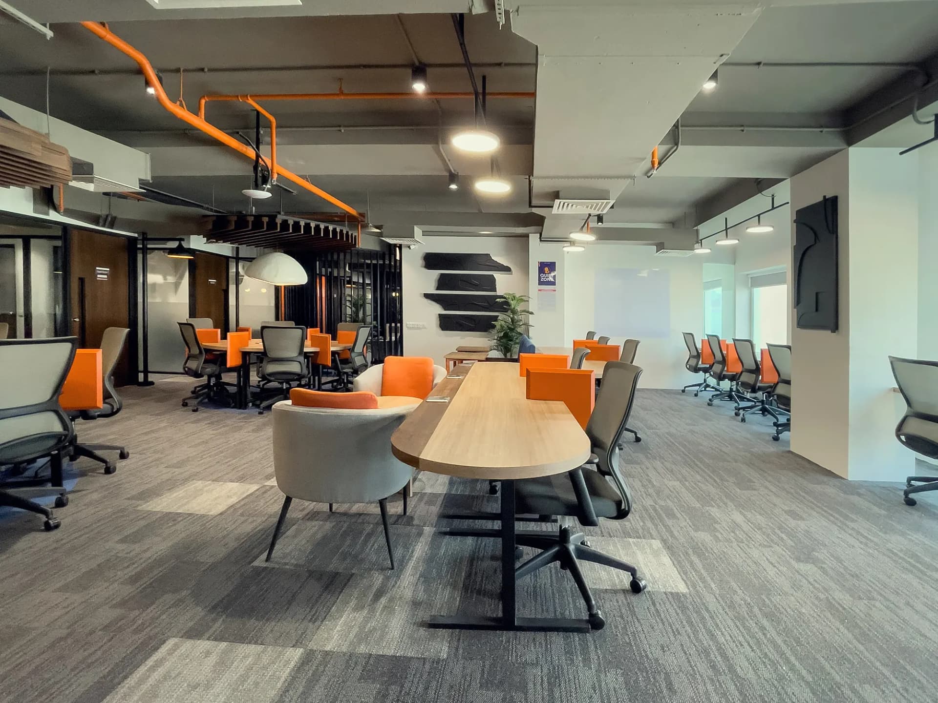 Open-plan desks at The Hive Karachi with orange chairs under exposed ceiling ducting